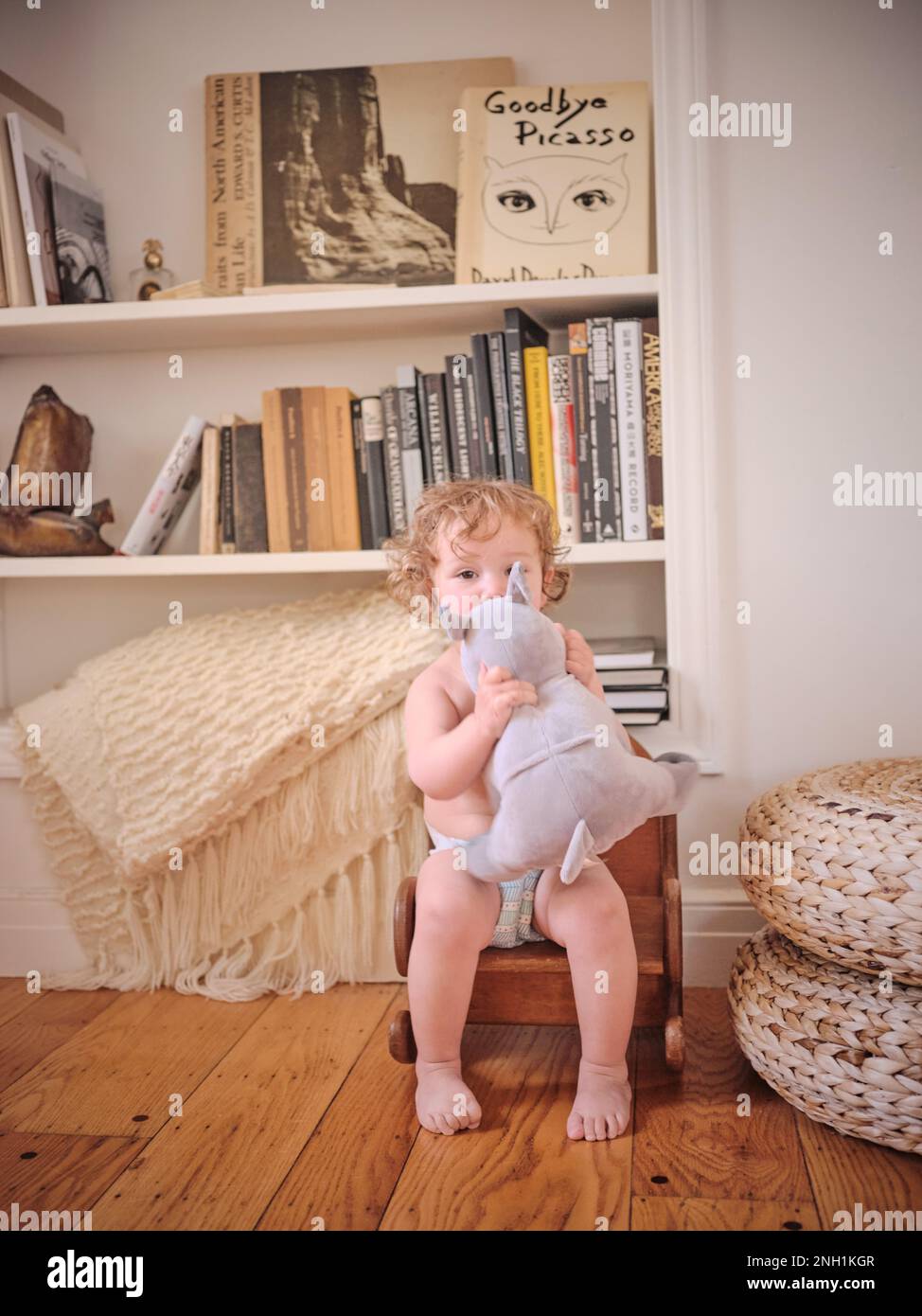 Il bimbo riccio si siede su una sedia a dondolo con un animale ripieno Foto Stock