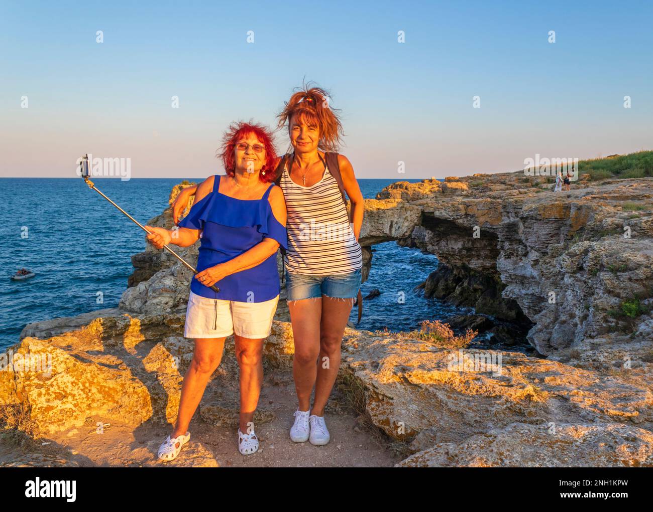 Donna anziana di 71 anni che tiene un bastone selfie che posa sorridendo con la sua figlia di 52 anni su una costa rocciosa, Tyulenovo, Bulgaria, agosto 2020 Foto Stock