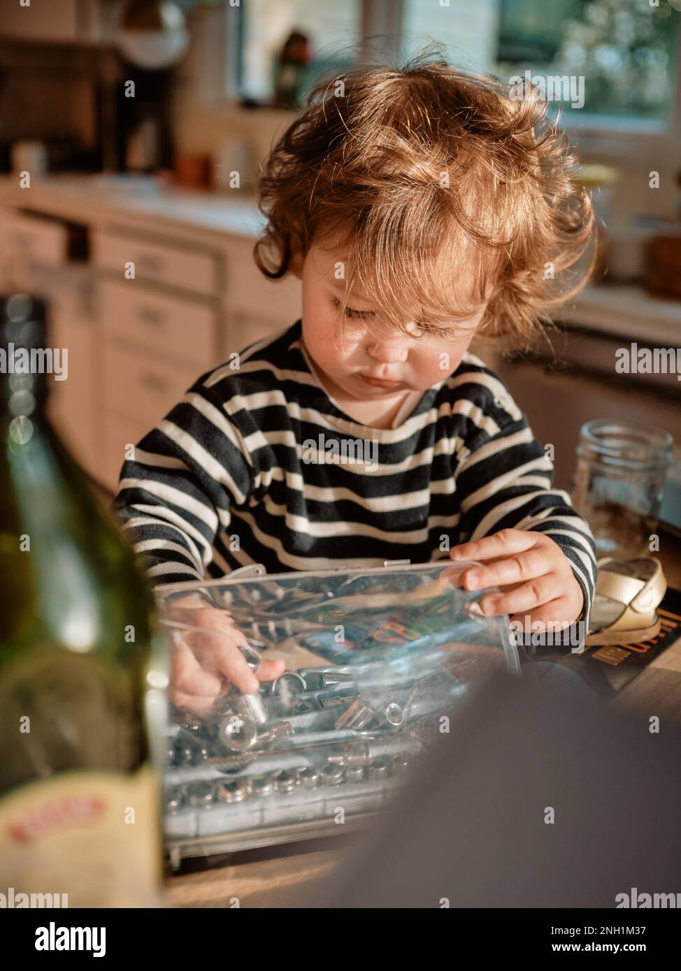 Il bambino con i capelli ricci rossi gioca con gli attrezzi in una cucina disordinata Foto Stock