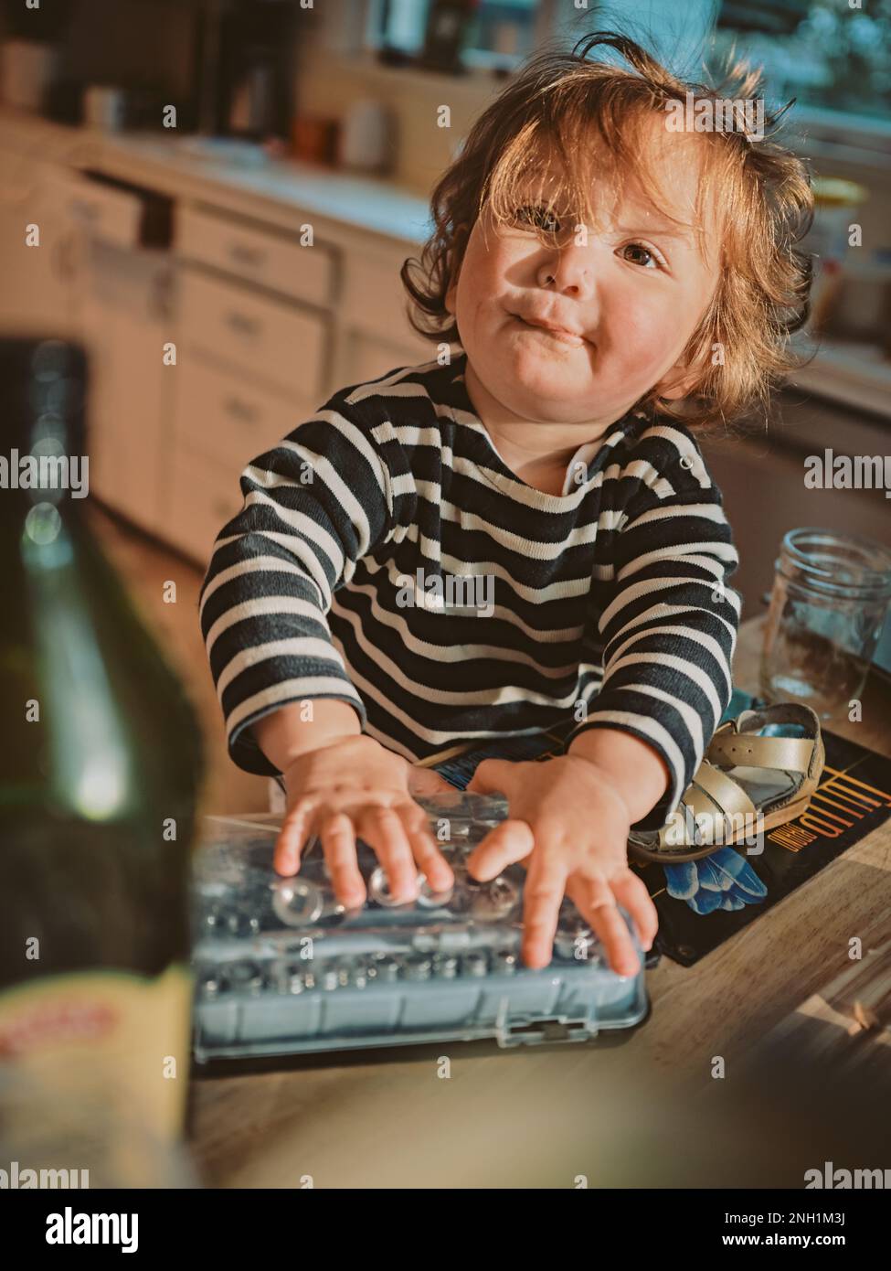 Il toddler fa un viso mentre gioca con un set di attrezzi in cucina Foto Stock