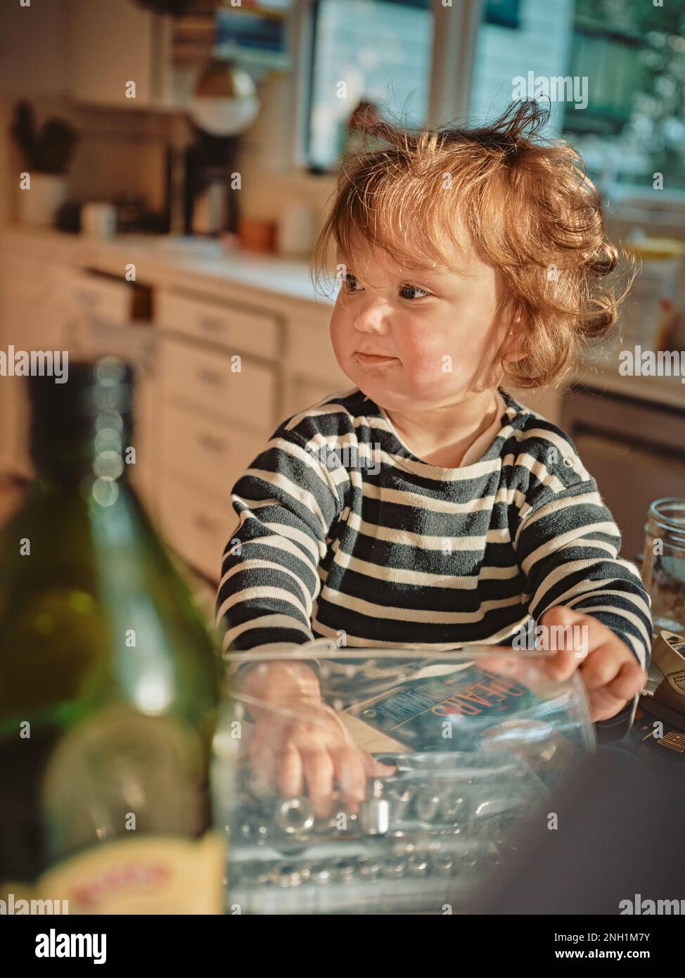 Il bambino che gioca con gli attrezzi guarda lontano in una cucina Foto Stock