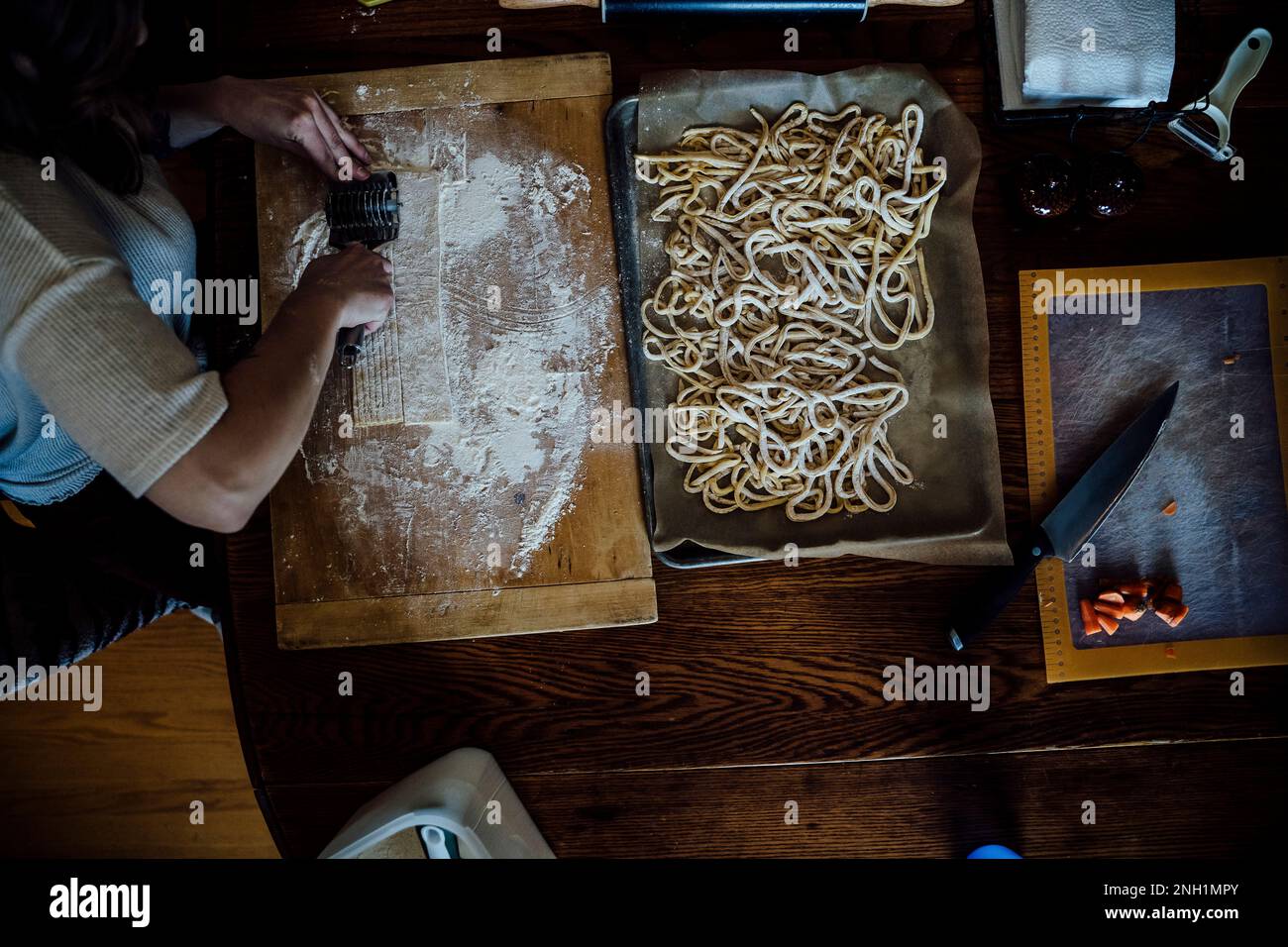 Vista dall'alto di Donna taglio di pasta fatta in casa sul tavolo da cucina Foto Stock