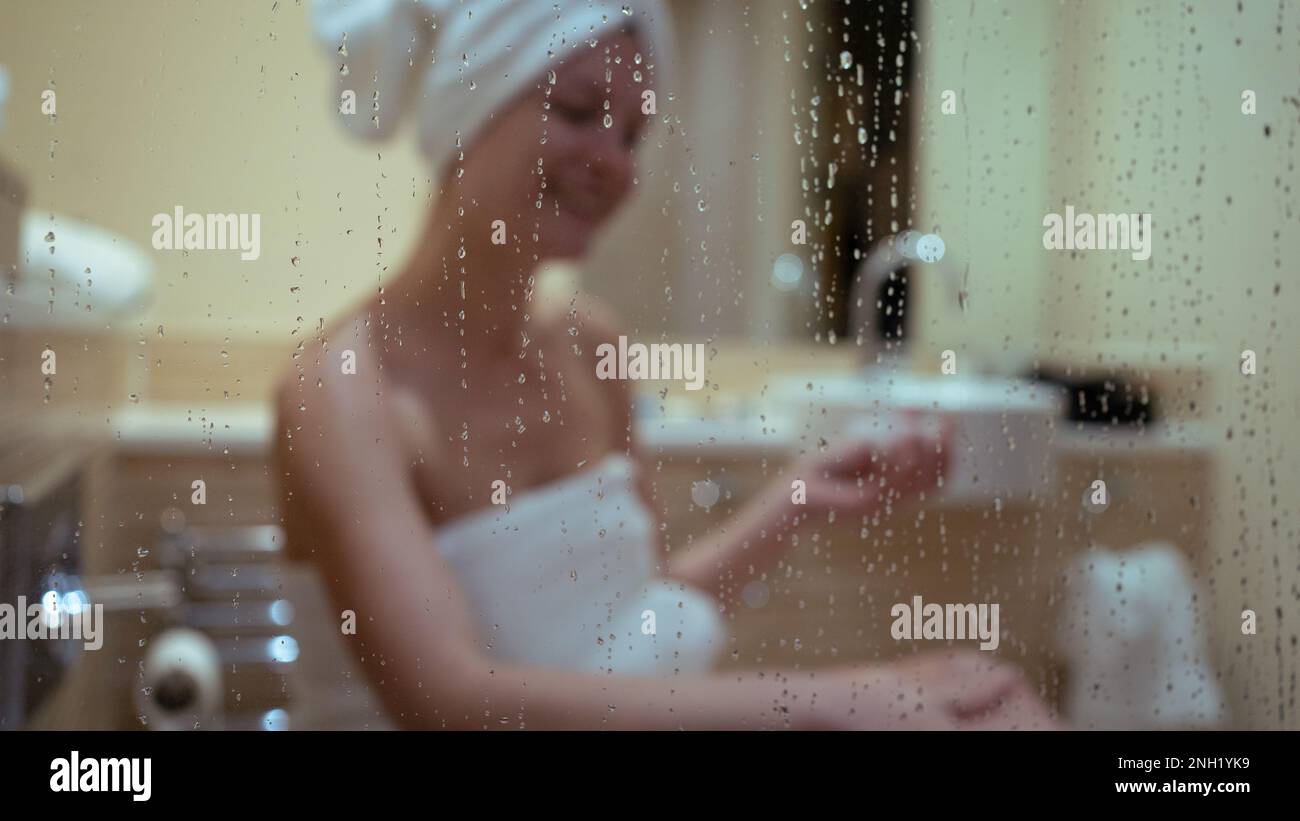 sfondo di una donna sorridente applicando una crema per il corpo nel bagno, bellezza di routine. a casa Foto Stock