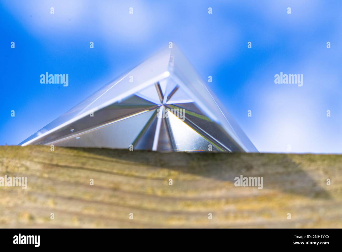 La parte inferiore di una piramide di cristallo seduto su una recinzione di legno con lo sfondo di un cielo nuvoloso blu, prospettiva Foto Stock