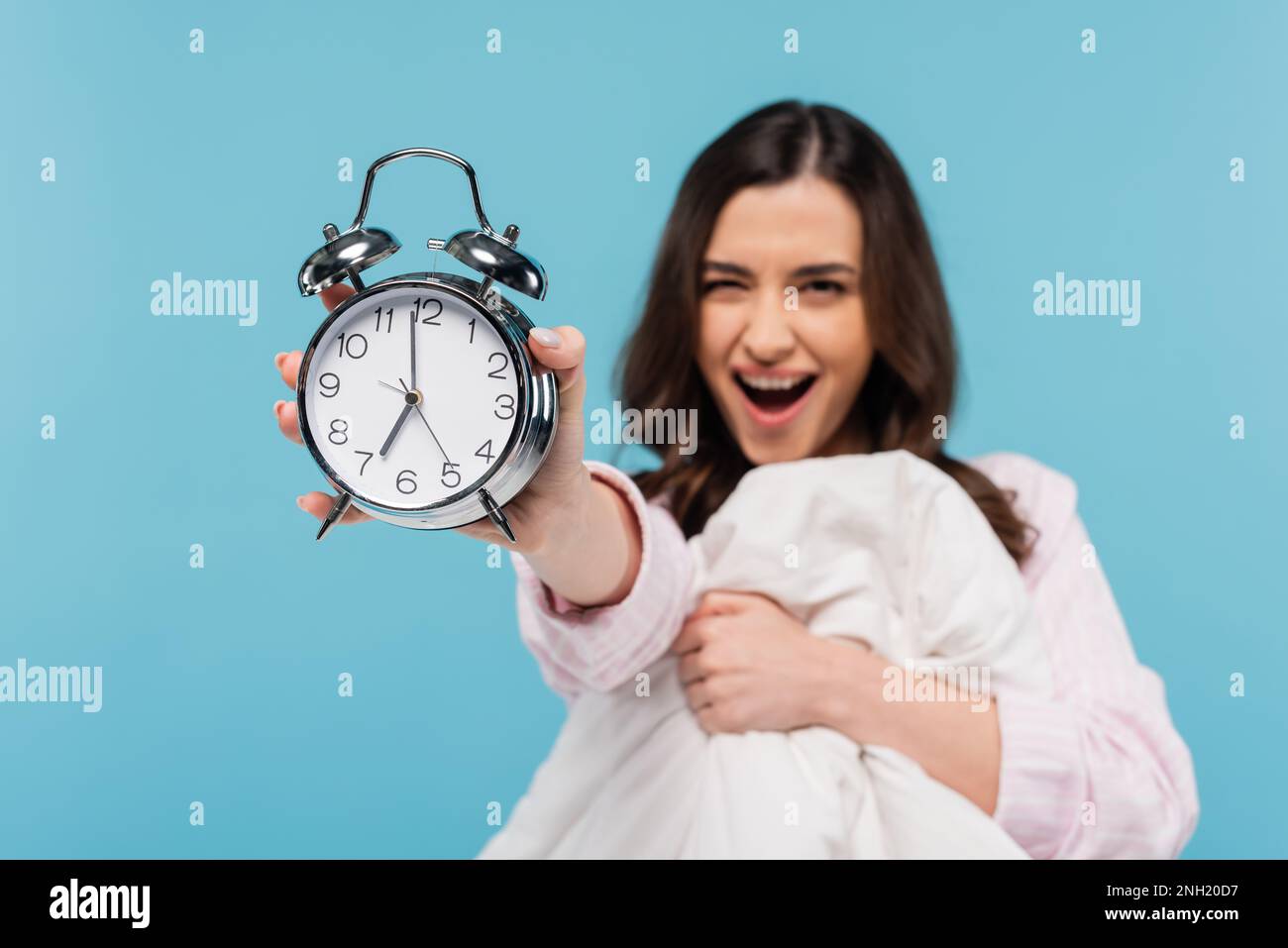 donna stupita in pigiama con sveglia vintage e piumino caldo isolato su blu, immagine stock Foto Stock