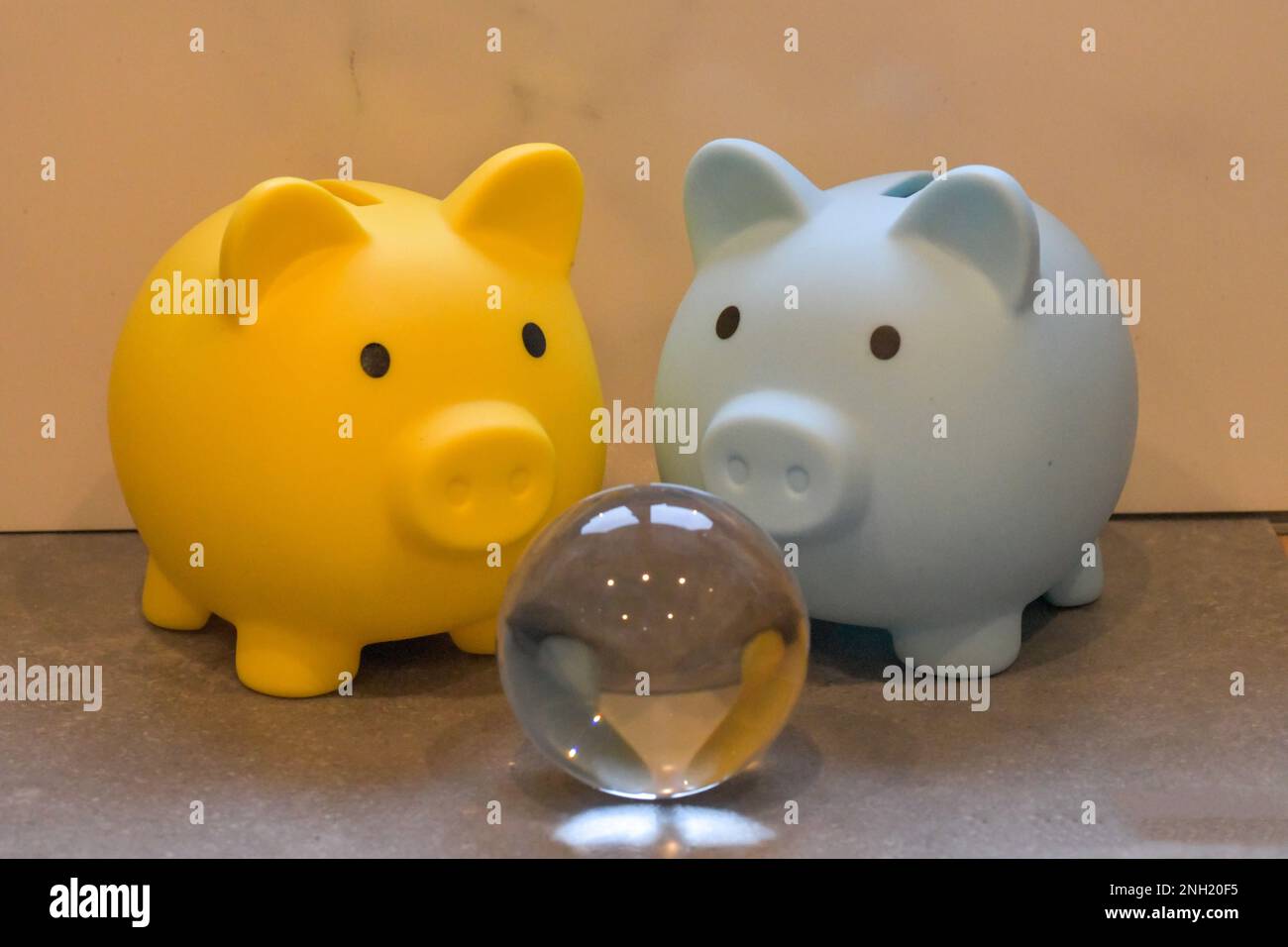 Un giallo e blu piggy banche che staring, guardando in una sfera di cristallo, futuro del denaro, investimenti futuri Foto Stock