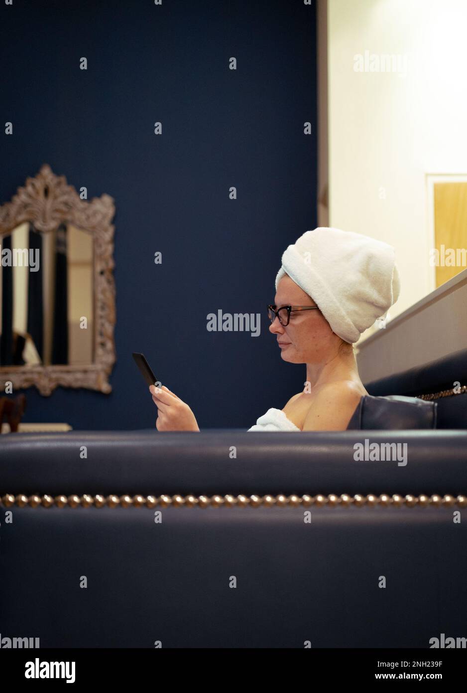 Ragazza giovane con gli occhiali che leggono un eBook rilassato dopo la doccia, routine di bellezza, a casa Foto Stock