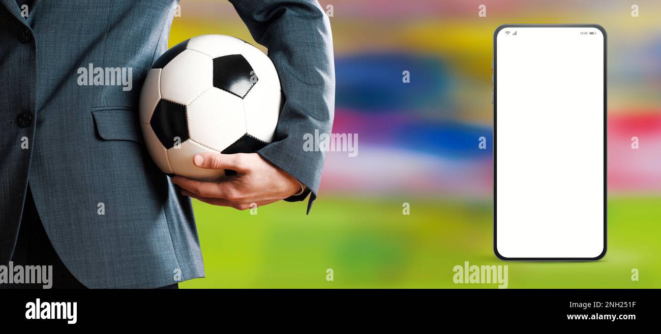 Manager che tiene una palla di calcio e app per smartphone, campo di calcio in background, concetto di app sportive e mobili Foto Stock