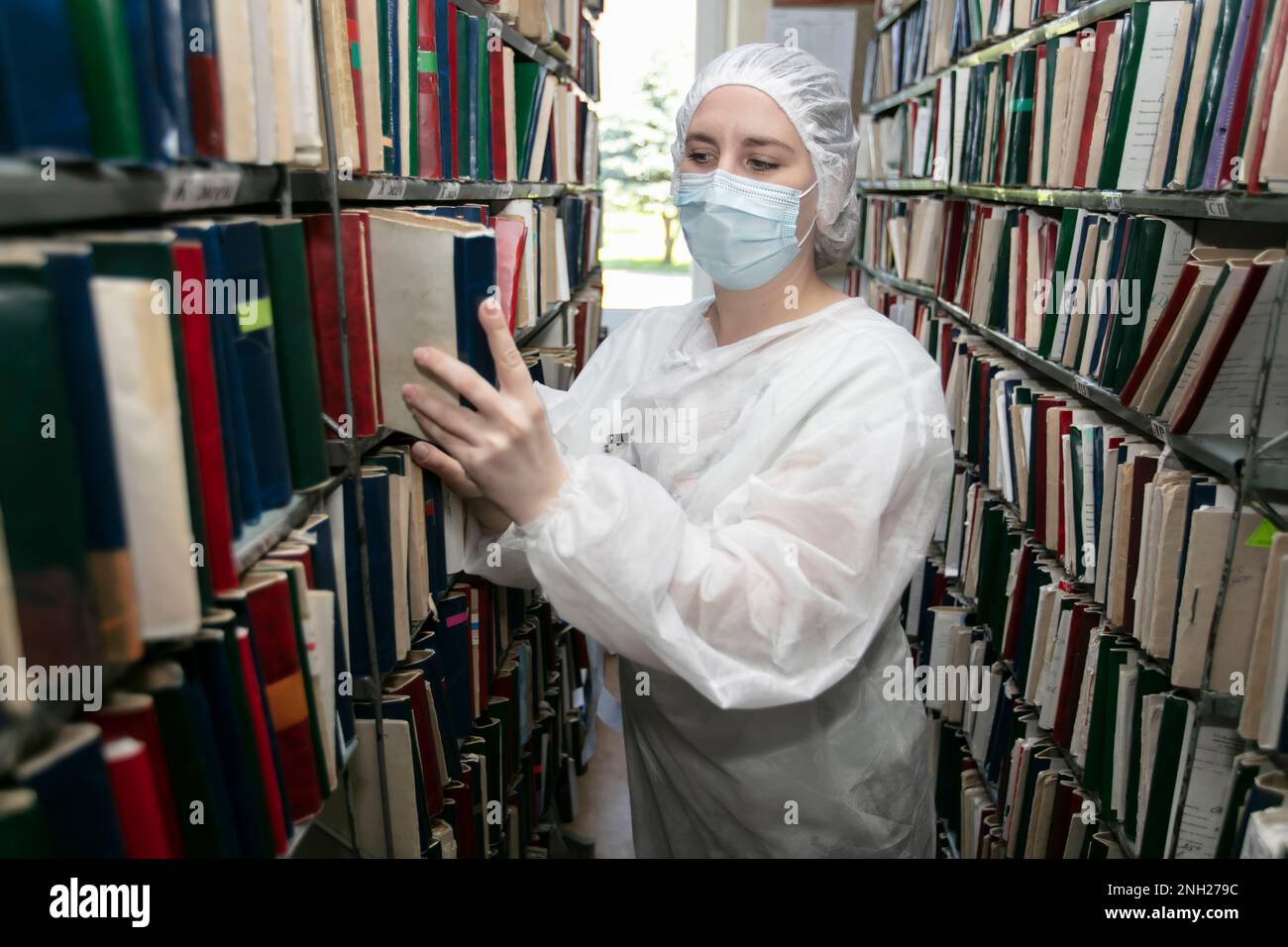 Una dottoressa in una divisa medica sullo sfondo di armadi con cartelle cliniche dei pazienti. Registro clinico. Elenco pazienti analogico. Foto Stock