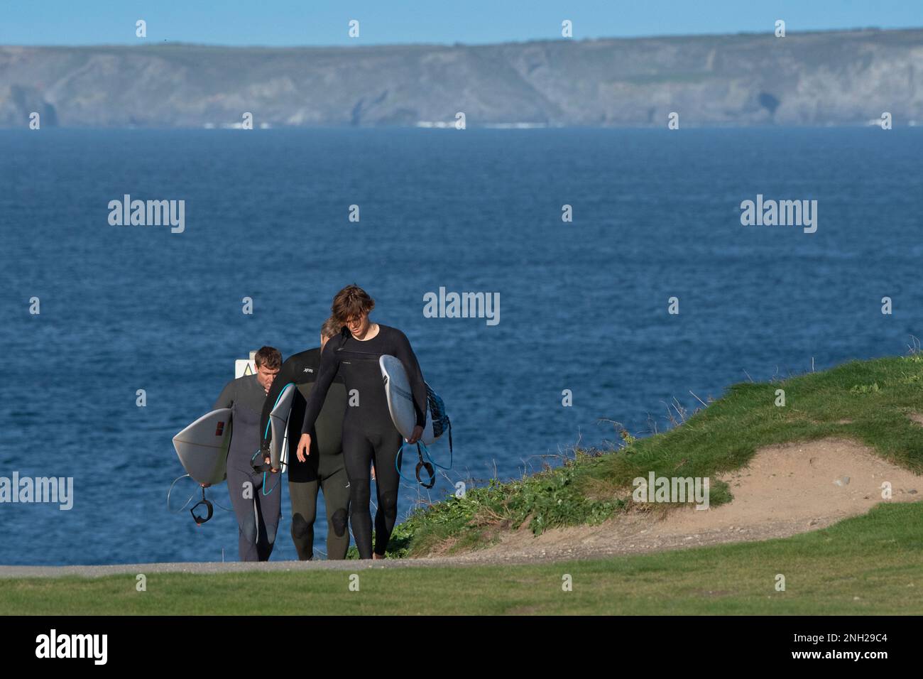 Tre surfisti che trasportano le loro tavole da surf e camminano lungo il sentiero costiero a Newequay in Cornovaglia in Inghilterra nel Regno Unito. Foto Stock