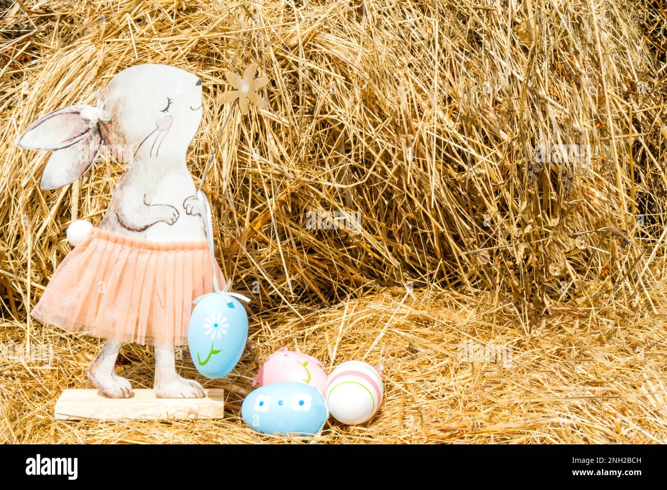 Un coniglio di legno in una bella gonna su fondo di fieno con uova di Pasqua dipinte. Pasqua, una cartolina con un posto per il testo. Foto di alta qualità Foto Stock