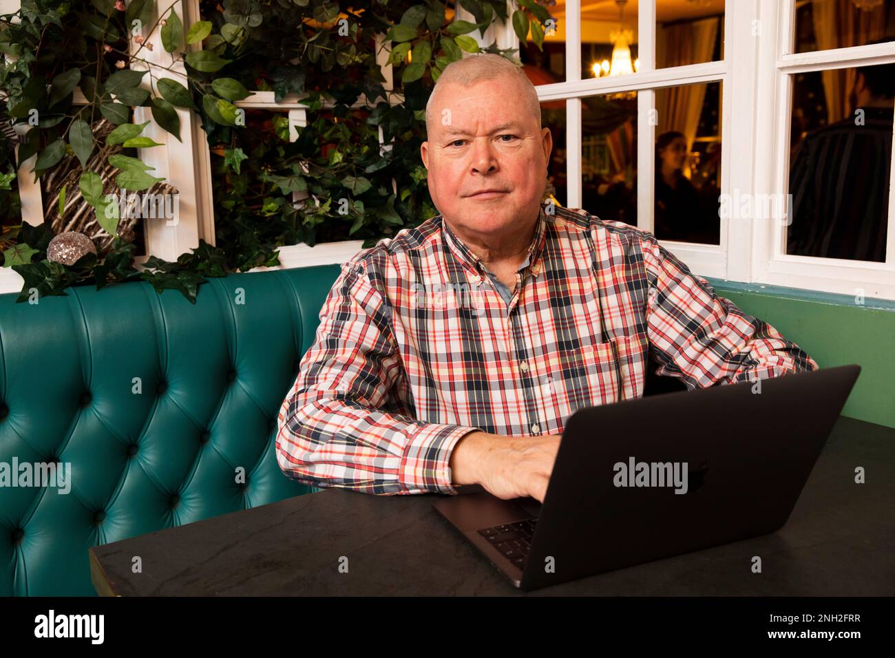 Uomo con 60s anni con un computer portatile seduto in un bar. Manchester. Regno Unito. Foto Stock