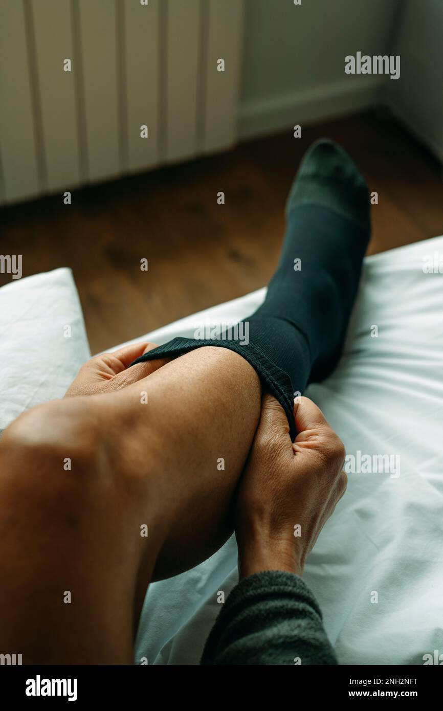 un uomo si mette su un calzino a compressione seduto sul letto di casa Foto Stock