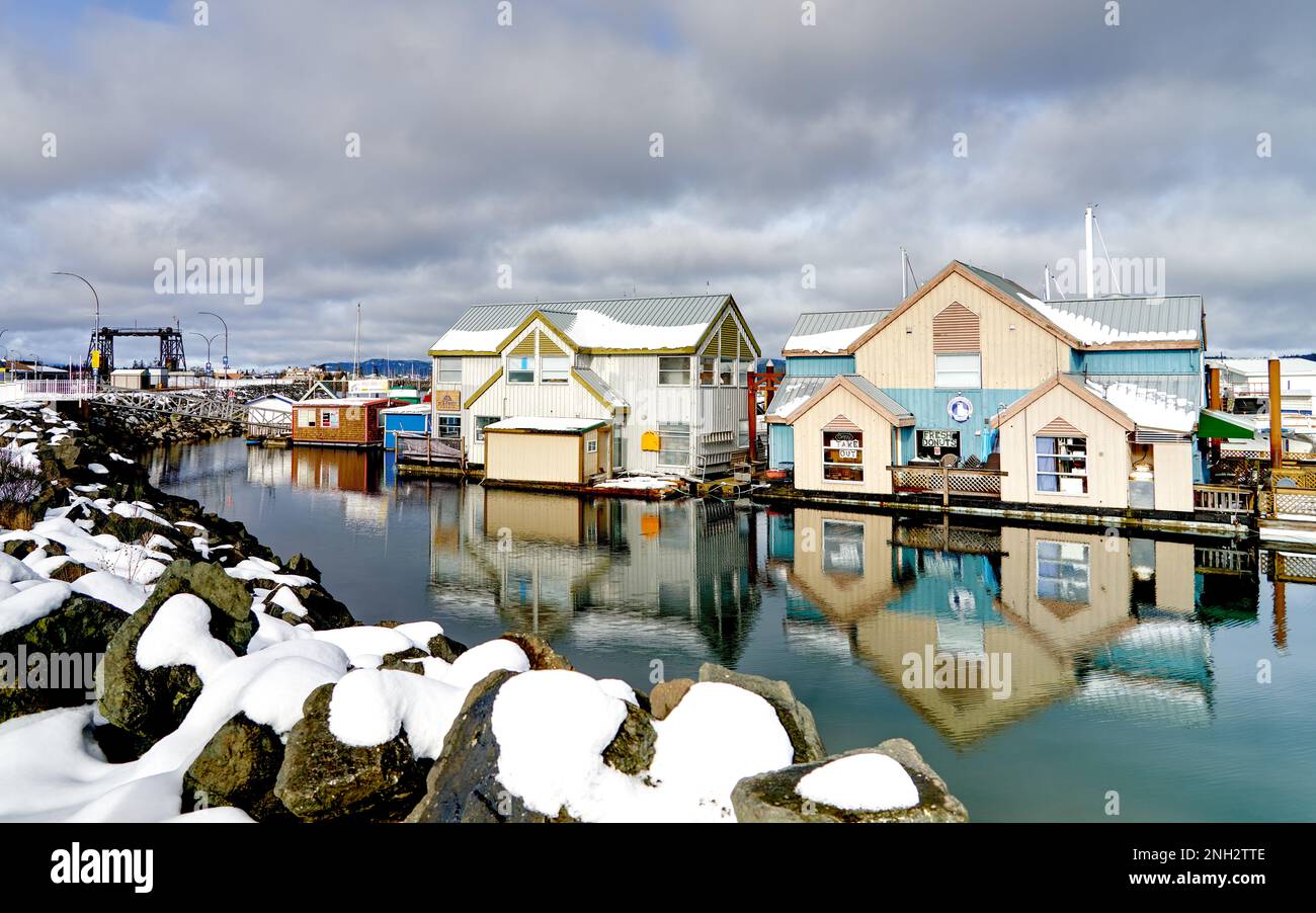 Edifici commerciali su galleggianti coperti di neve e i loro riflessi nella tranquilla acqua dell'oceano in una luminosa giornata invernale. Foto Stock