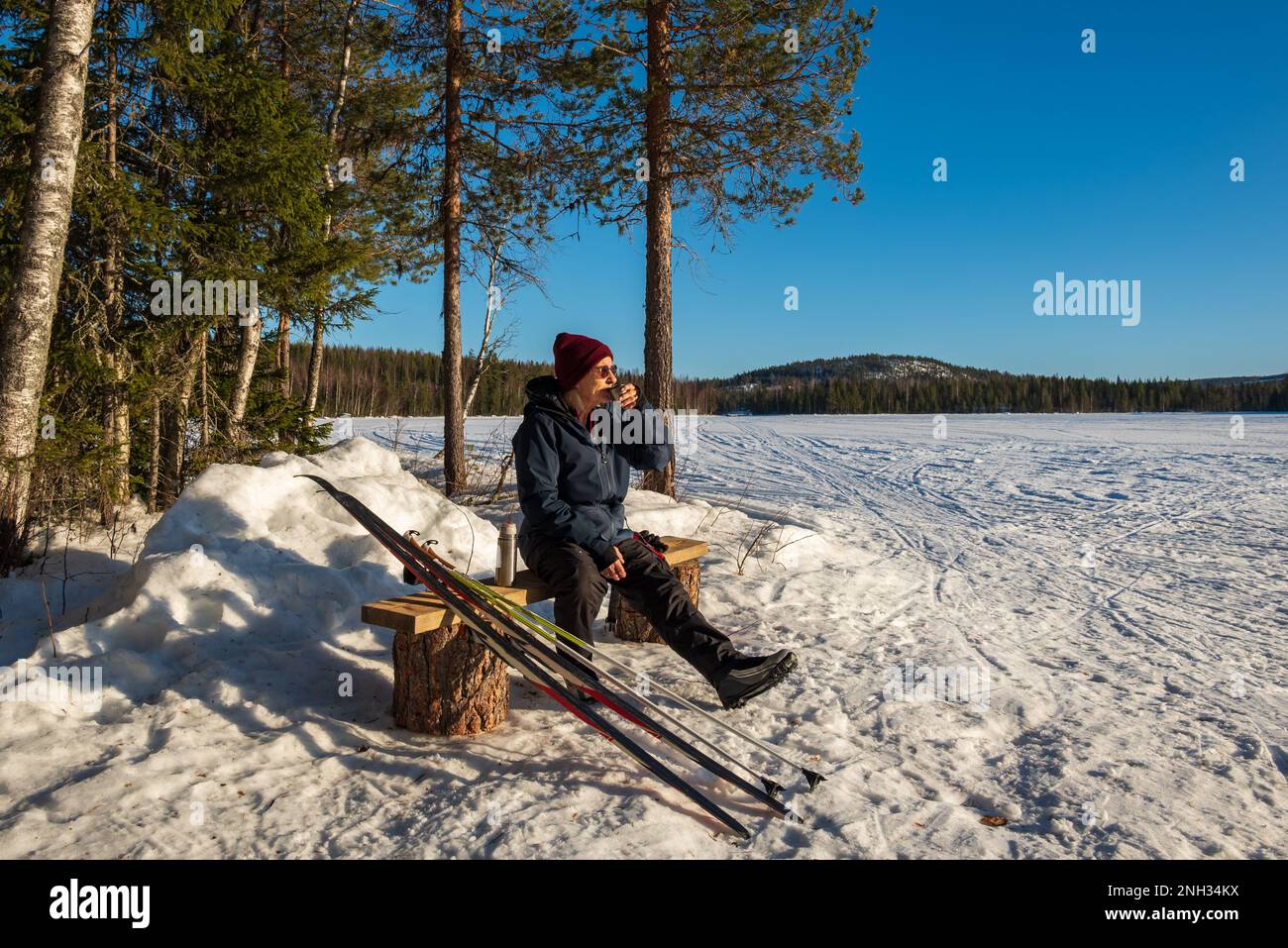 Una donna anziana riposa dopo aver sciato e beve una tazza di caffè e gode del sole, immagine dalla Svezia vasternorrland. Foto Stock