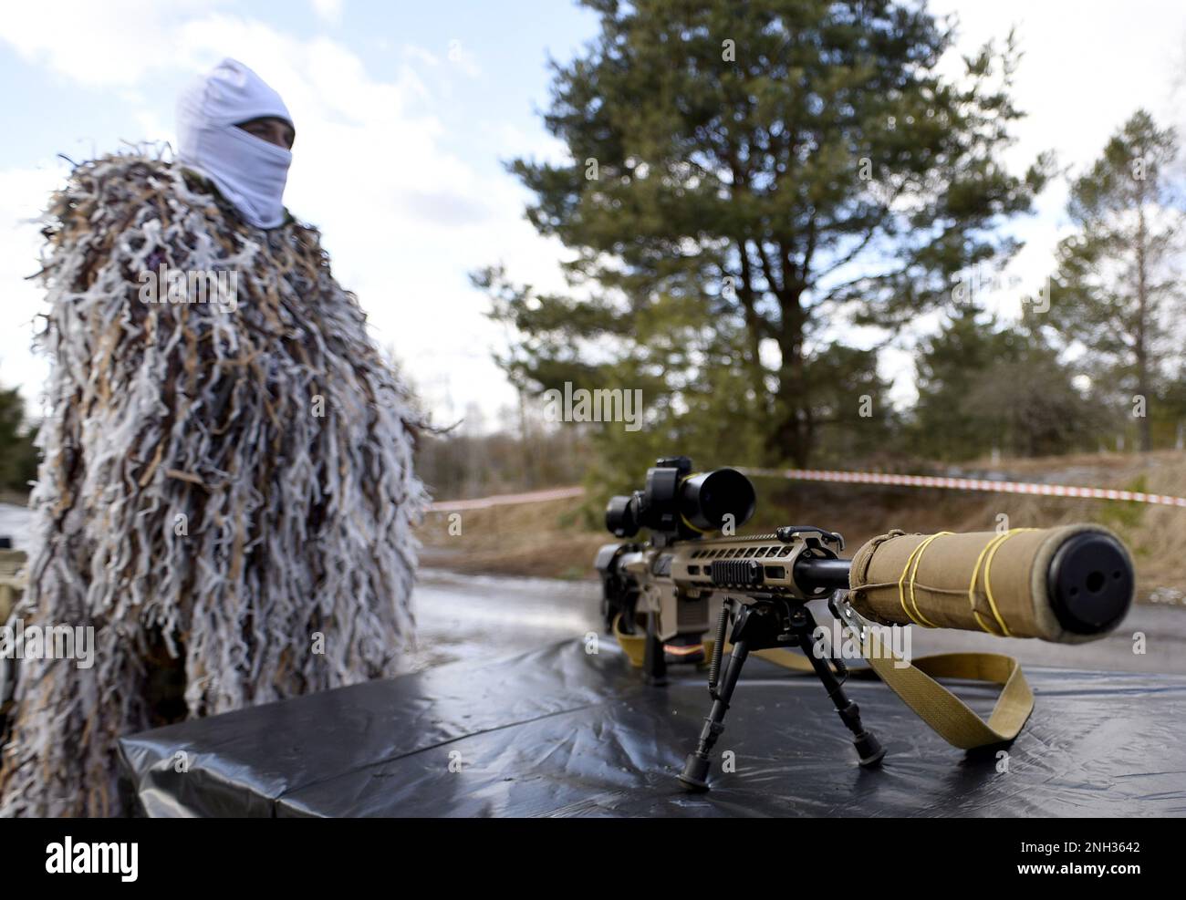 REGIONE DI KYIV, UCRAINA - 20 FEBBRAIO 2023 - Un serviceman ucraino in una tuta di ghillie d'inverno si alza da un fucile da cecchino durante un esercizio militare su larga scala Foto Stock