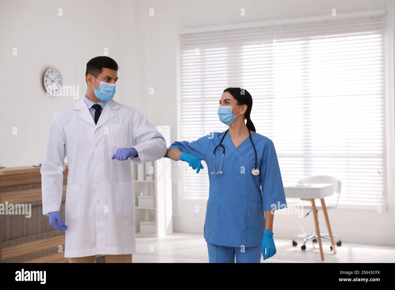 I medici con maschere protettive si salutano a vicenda saltando i gomiti invece di stretta di mano in clinica Foto Stock