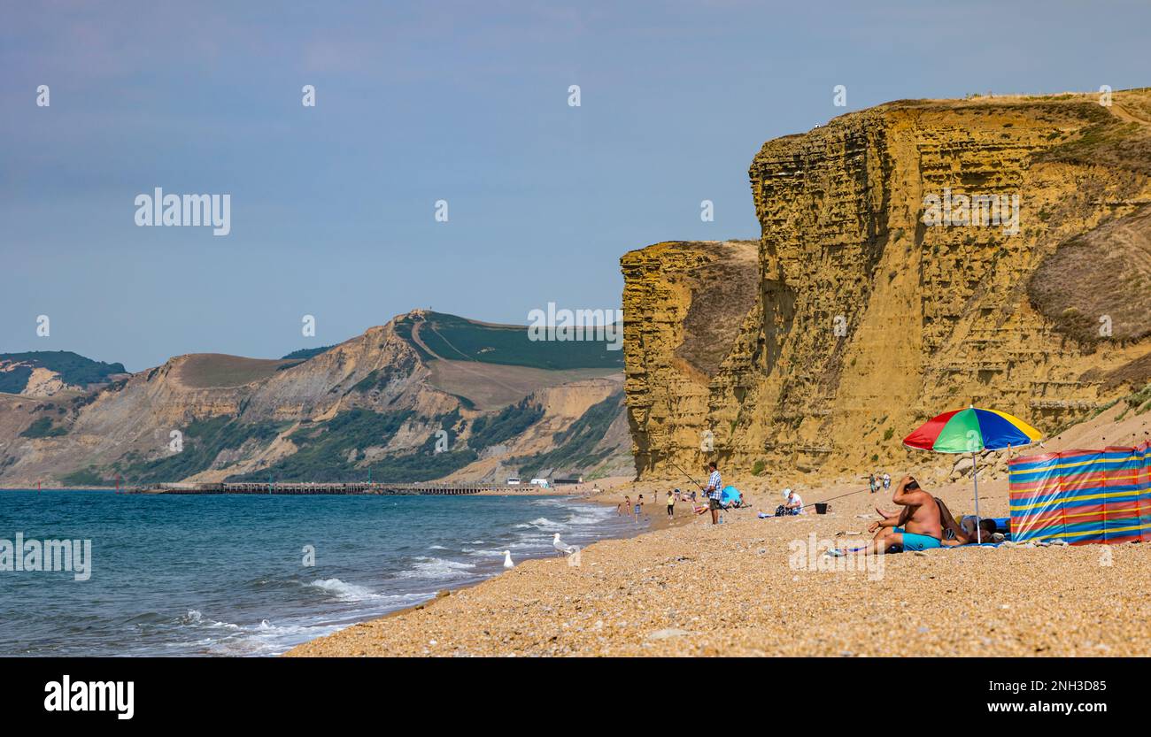 Persone che prendono il sole sulla spiaggia sotto scogliere calcaree, Jurassic Coast, Burton Freshwater, Dorset, Inghilterra, REGNO UNITO Foto Stock