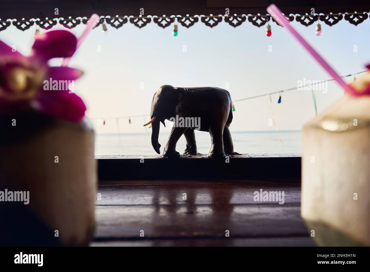 Decorazione con statue di elefanti in legno del resort presso la spiaggia tropicale all'alba con due palme da cocco in primo piano sul tavolo Foto Stock