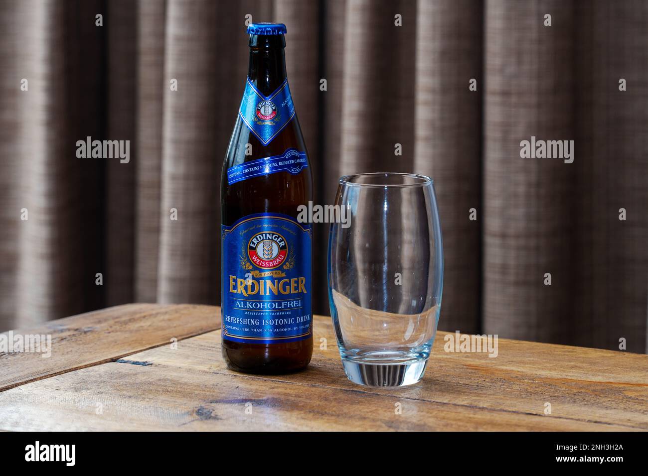 Una bottiglia di birra Erdinger Weissbrau senza alcool su un tavolo, con un bicchiere pulito e vuoto accanto. Foto Stock