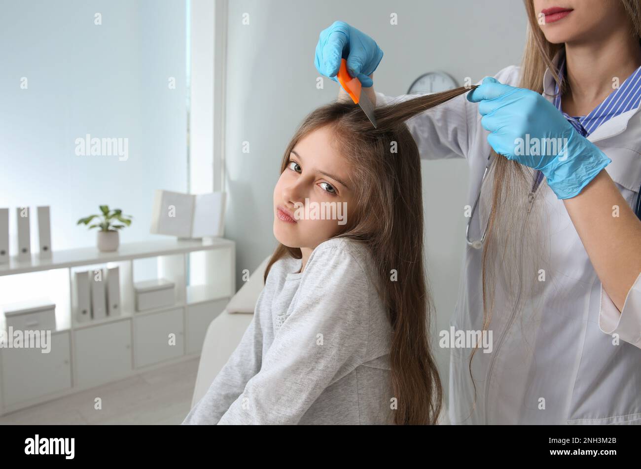 Medico che usa il pettine nit sui capelli della ragazza in clinica. Trattamento antighiaccio Foto Stock