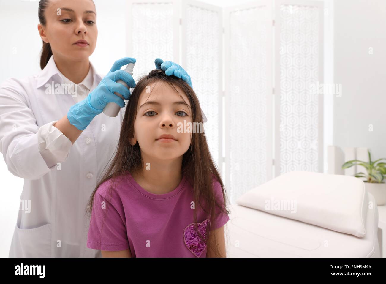 Medico che usa lo spray trattamento pidocchi sui capelli della bambina all'interno Foto Stock