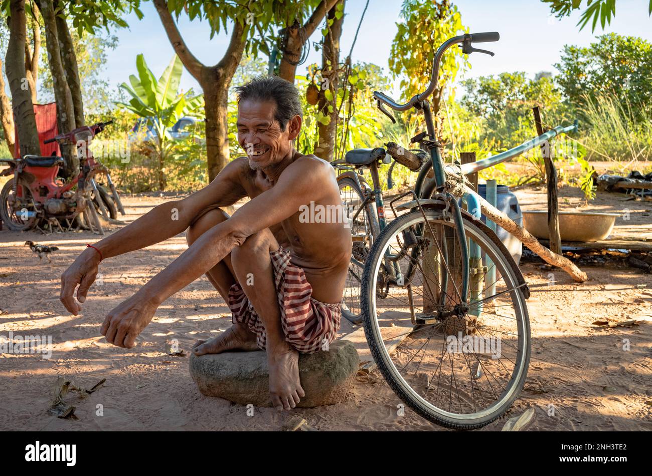 Un uomo di mezza età si schiaccia su una grande pietra accanto alla sua bicicletta in un villaggio vicino a Siem Reap in Cambogia. Foto Stock