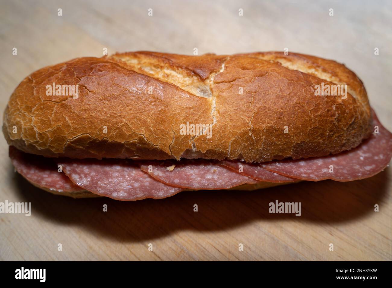 Baguette croccante con fette di salame su un asse di legno Foto Stock