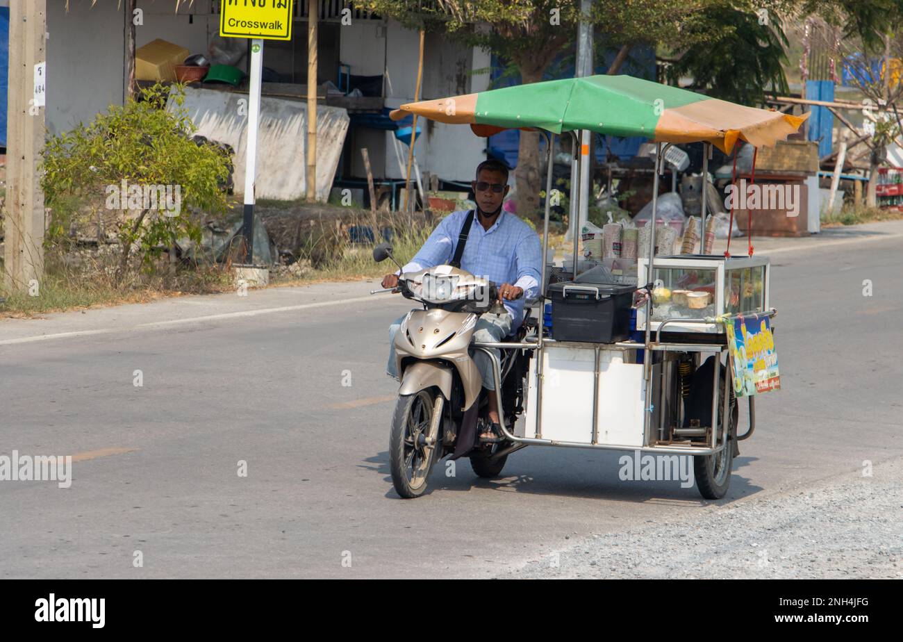 SAMUT PRAKAN, THAILANDIA, 01 2023 FEBBRAIO, un distributore di gelati cavalca una motocicletta a tre ruote lungo una strada del villaggio, Thailandia Foto Stock