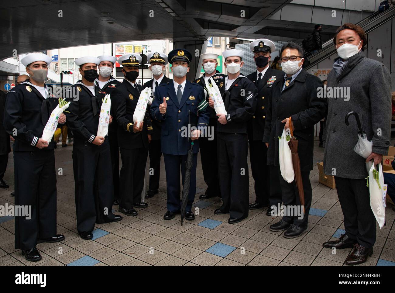 YOKOSUKA, Giappone (13 dicembre 2022) — i marinai assegnati al comandante, le attività della flotta Yokosuka (CFAY) e i dipendenti civili della CFAY posano con il commissario aggiunto Kazuo Katoh, capo della stazione di polizia di Yokosuka per una foto di gruppo durante un evento che aumenta la consapevolezza della guida ubriaca durante la stagione delle festività. L'evento, tenuto in collaborazione con la stazione di polizia di Yokosuka e con le altre organizzazioni di sicurezza di Yokosuka, prevede la distribuzione di raggiera di daikon giapponesi ai pedoni. "Daikon" è un gioco di parole in quanto è vicino alla parola giapponese "daikonzetsu", che significa sradicamento (della guida ubriaca) Foto Stock