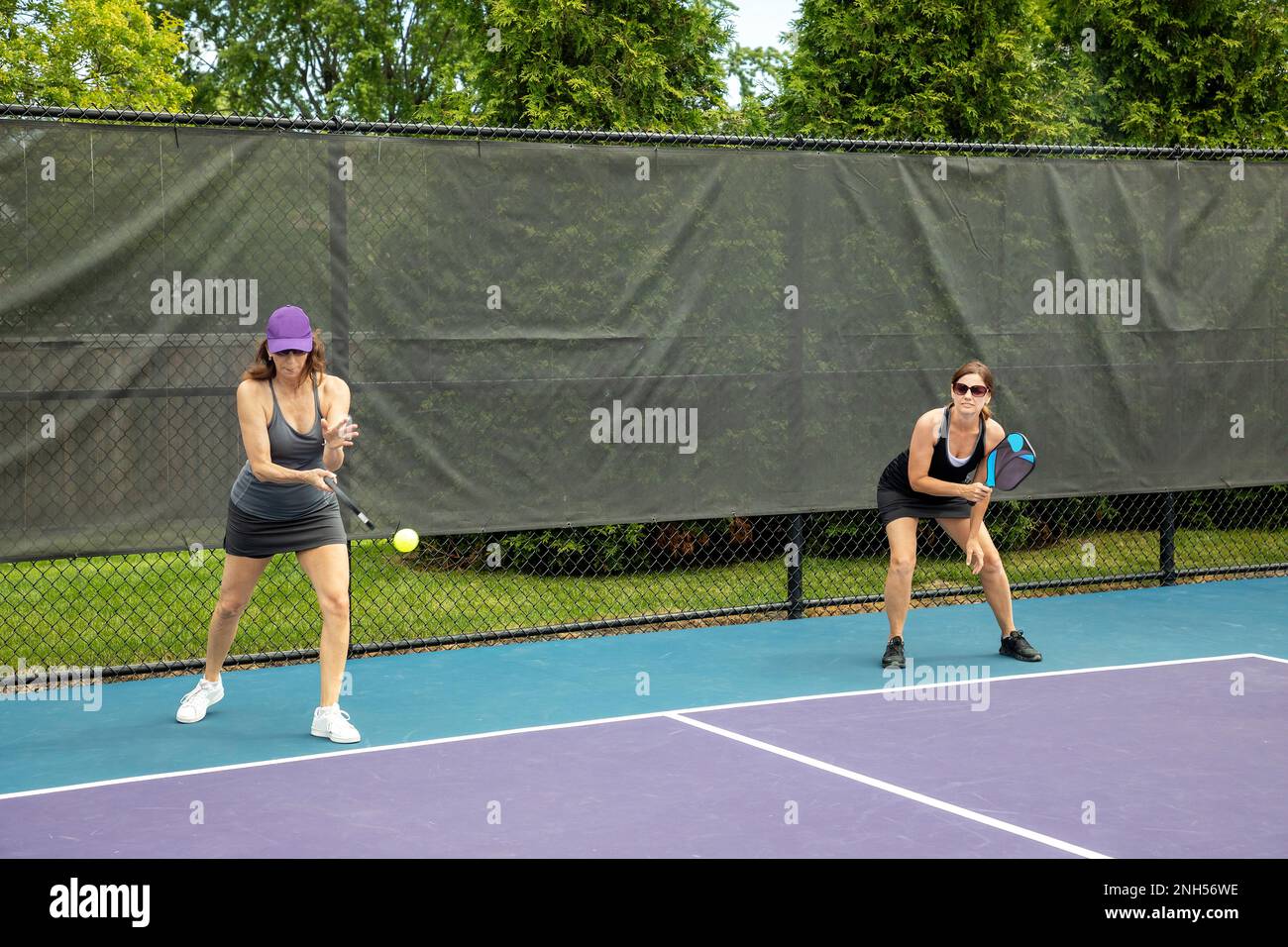 Un giocatore di pickleball serve il pallone come il suo compagno guarda. Foto Stock