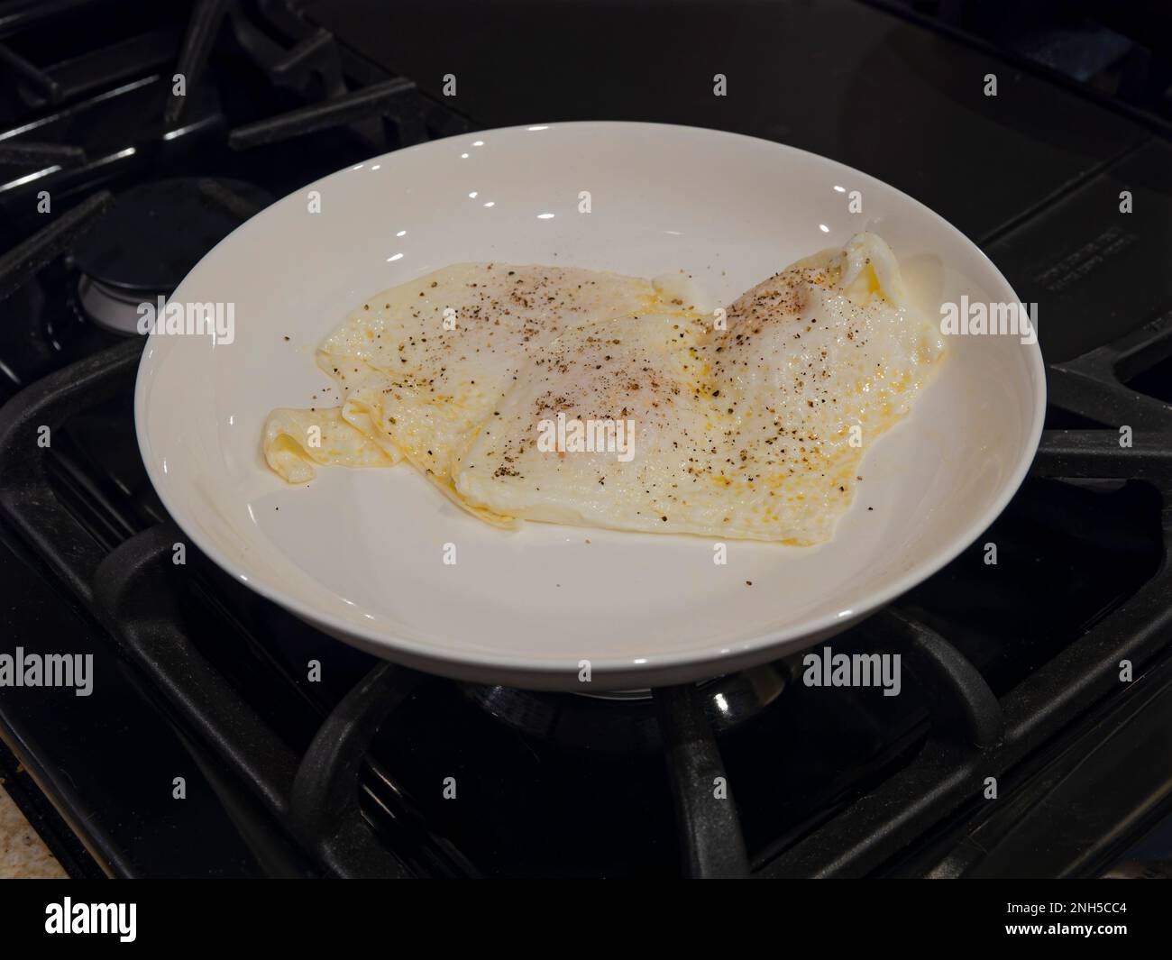 Uova fritte su media superficie, per colazione, in un piatto da pranzo bianco su un piano cottura. Foto Stock