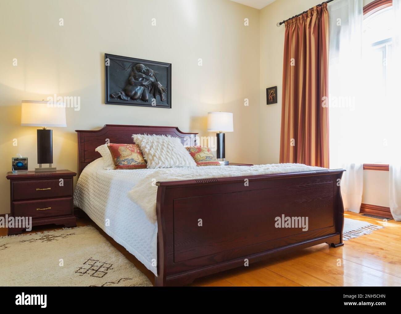 Comodino e letto queen size con testata in legno e poggiapiedi in camera da letto al piano superiore all'interno di una lussuosa casa. Foto Stock