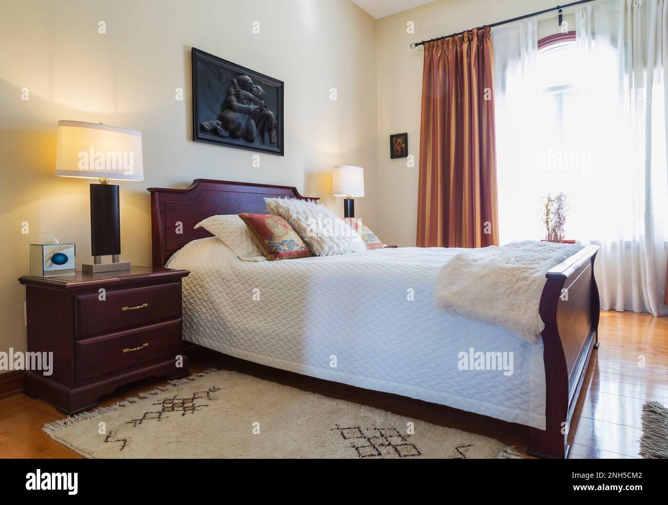 Comodino e letto queen size con testata in legno e poggiapiedi in camera da letto al piano superiore all'interno di una lussuosa casa. Foto Stock