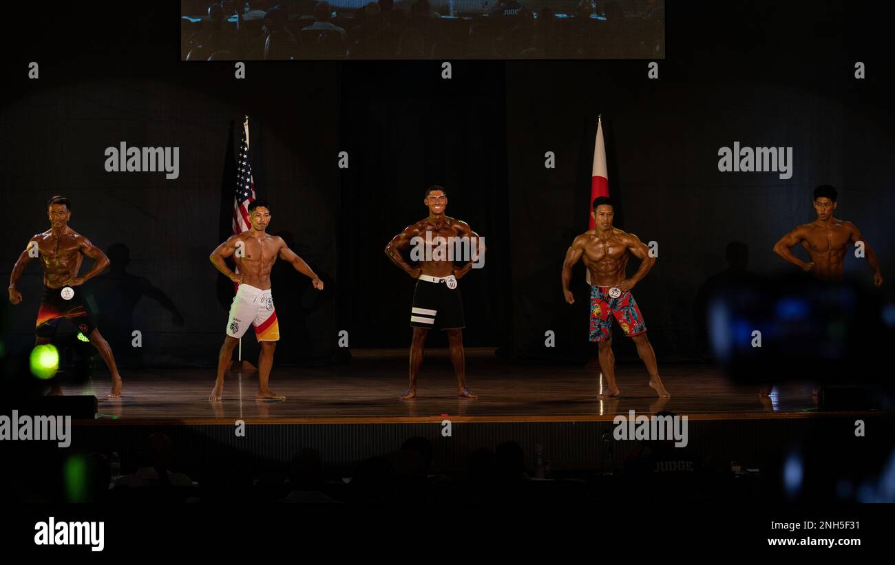 I concorrenti si esibiscono in prima fila alla Estremo Oriente Bodybuilding Competition 2022, divisione Physique maschile a Camp Foster, Giappone, 17 luglio 2022. Per questa divisione, i giudici cercano un fisico moderatamente magro e muscolare, e giudicano gli stili generali dei capelli, i capelli, l'abbigliamento e la posa. Foto Stock