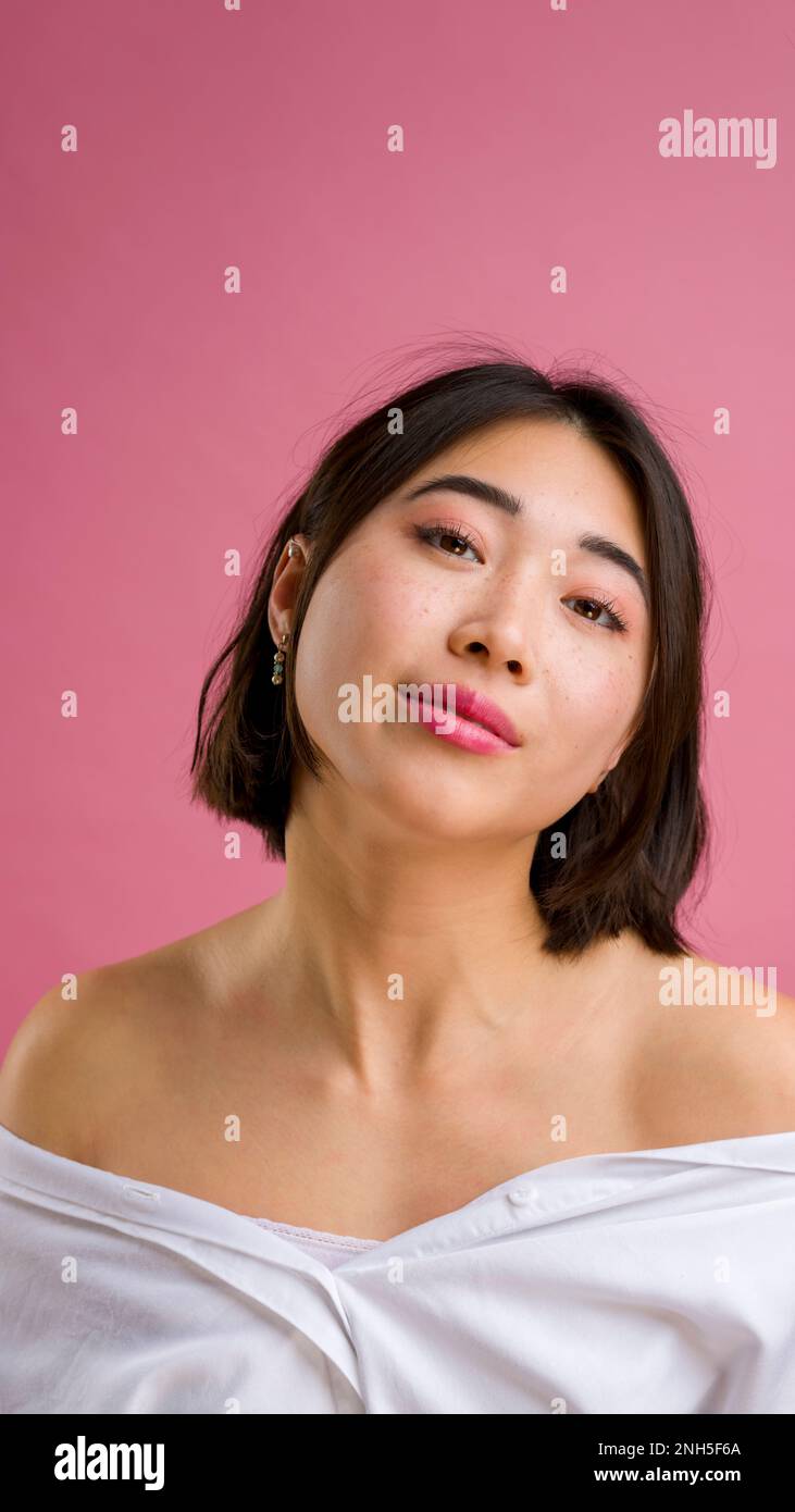 Primo piano di giovane donna asiatica con short in blusa bianca su sfondo rosa | trucco | moda Foto Stock