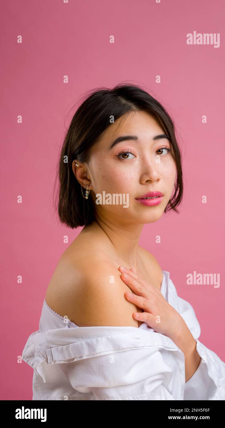 Primo piano di giovane donna asiatica con short in blusa bianca su sfondo rosa | trucco | moda Foto Stock