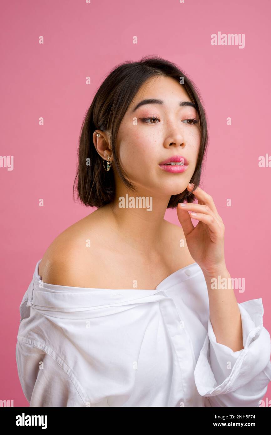 Primo piano di giovane donna asiatica con short in blusa bianca su sfondo rosa | trucco | moda Foto Stock