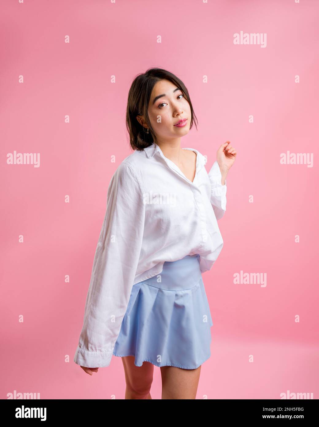 3/4 Body Asian Woman Standing Camera fronte Bianco Blouse Blue Short gonna fronte Camera Rosa sfondo | copy space Foto Stock