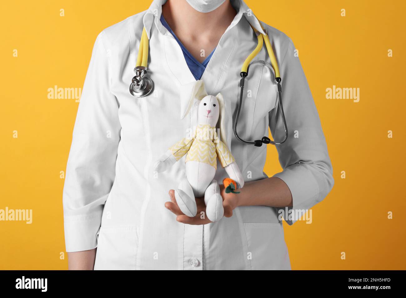 Pediatra con coniglio giocattolo e stetoscopio su sfondo giallo, primo piano Foto Stock