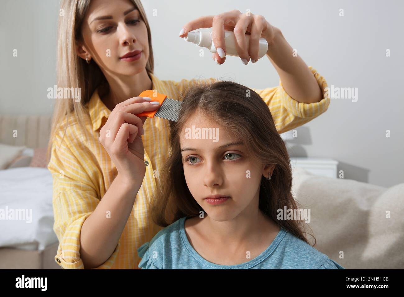 Madre usando nit pettine e spray sui capelli della figlia a casa. Trattamento antighiaccio Foto Stock