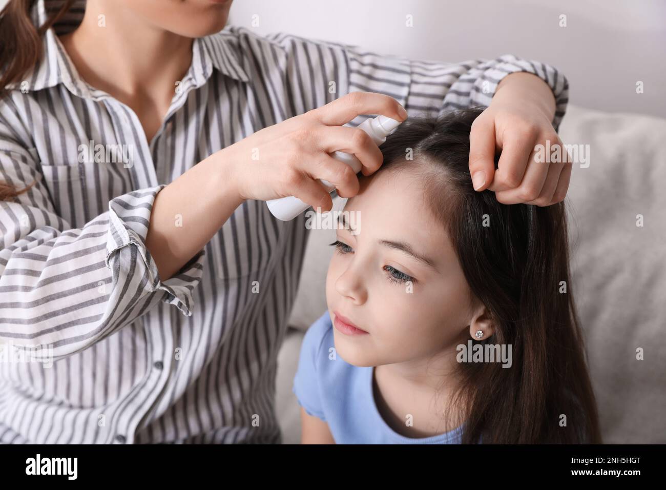 Madre che usa lo spray trattamento pidocchi sui capelli di sua figlia all'interno Foto Stock