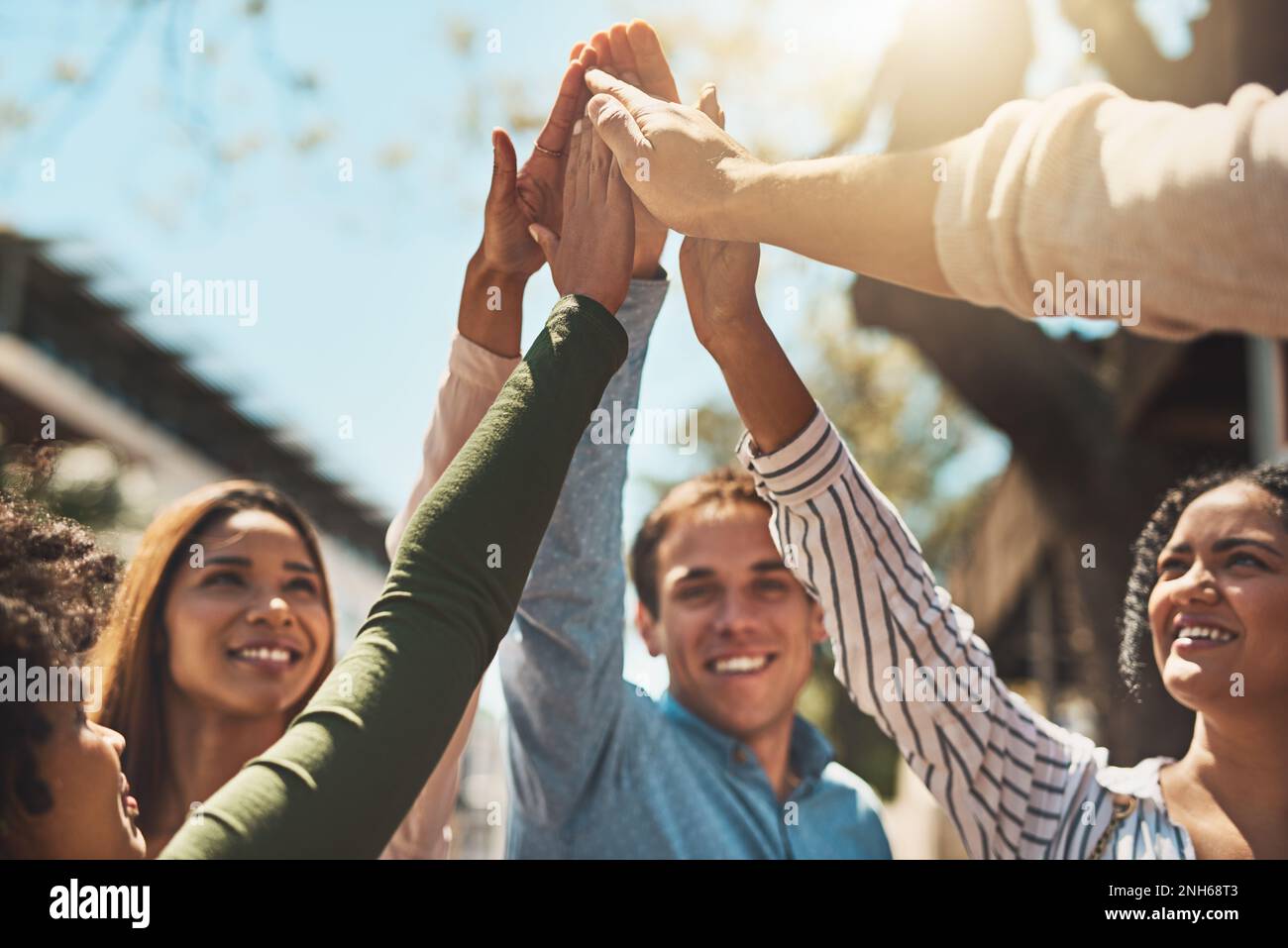 Heres ad un giorno impressionante davanti a noi. un gruppo di giovani amici allegri che formano una huddle e si danno a vicenda un alto cinque fuori durante il giorno. Foto Stock