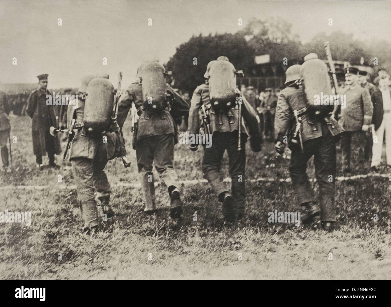 1914-1918. Prima guerra mondiale quattro soldati tedeschi completamente equipaggiati con uniforme, casco in acciaio e con lanciafiamme sulla schiena che corrono una corsa. Potete vedere gli uomini da dietro appena prima della linea di arrivo. Sullo sfondo e sui lati sono visibili gli spettatori. Foto Stock