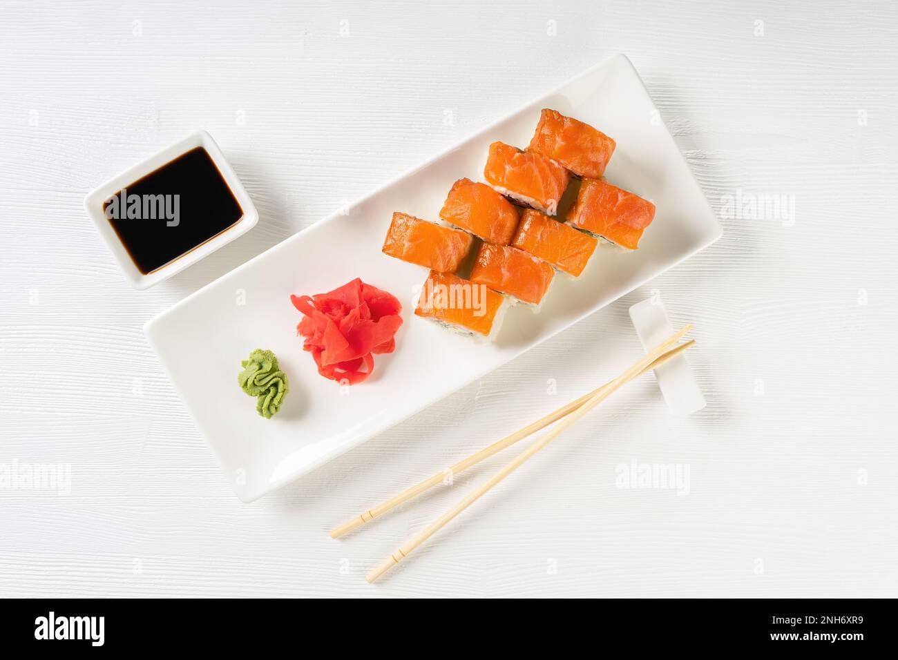 Filadelfia di sushi con salmone, anguilla affumicata, avocado, formaggio cremoso su sfondo bianco. Menu di sushi, panini serviti su piatto bianco con wasabi, zenzero Foto Stock