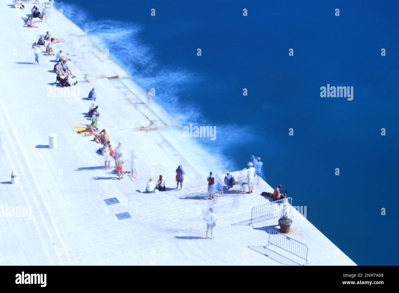 Un gruppo di persone si è riunito su un molo di pietra, che si affaccia su un tranquillo corpo d'acqua Foto Stock