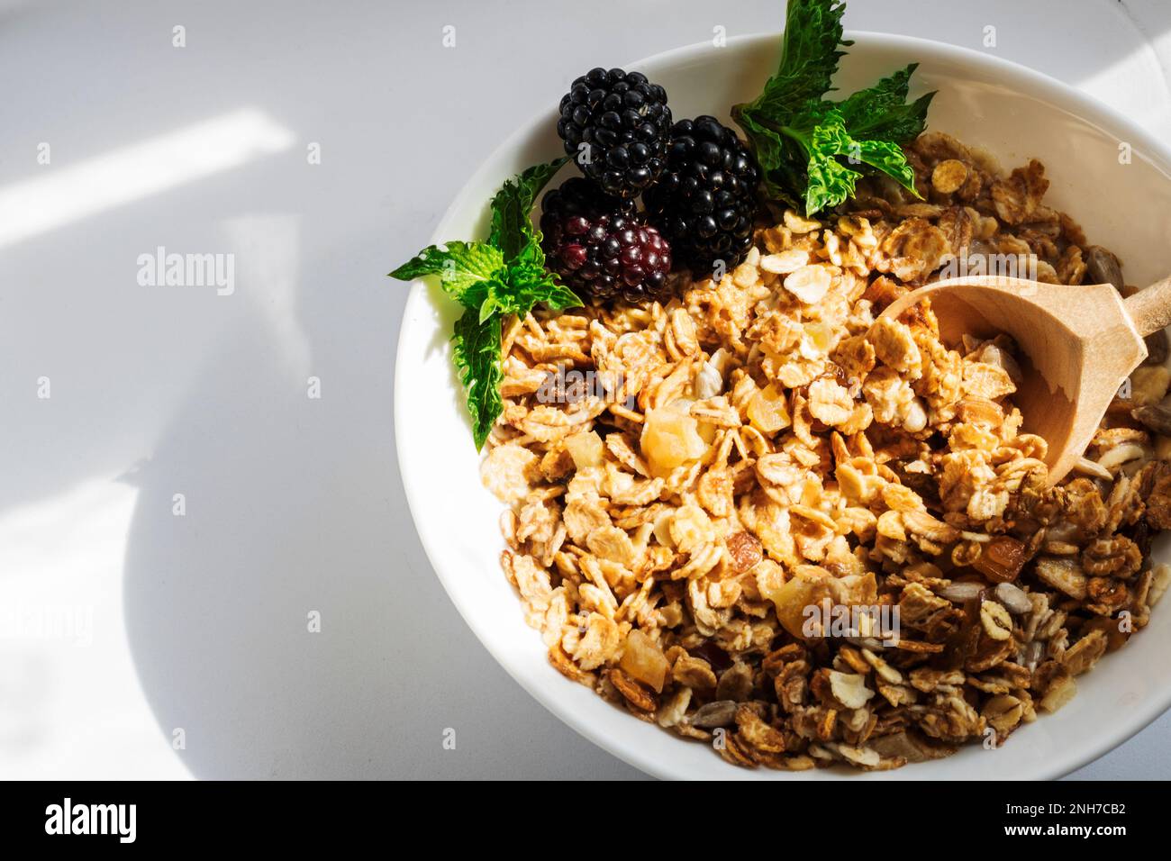 Mora con foglie di menta, in un piatto di granola con latte, su fondo bianco con ombre dure. Messa a fuoco selettiva. Spazio di copia Foto Stock