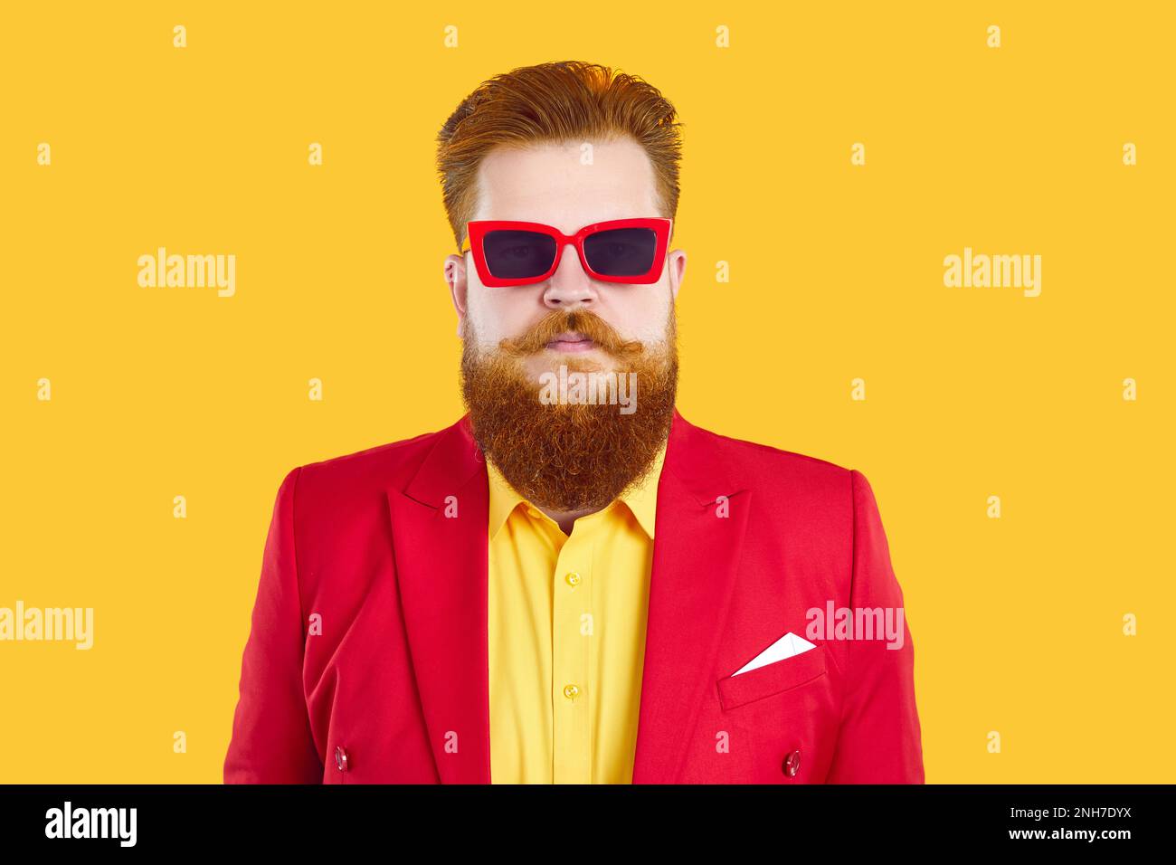 Ritratto di divertente uomo bearded serio in tuta rossa, camicia gialla e occhiali da sole funky Foto Stock