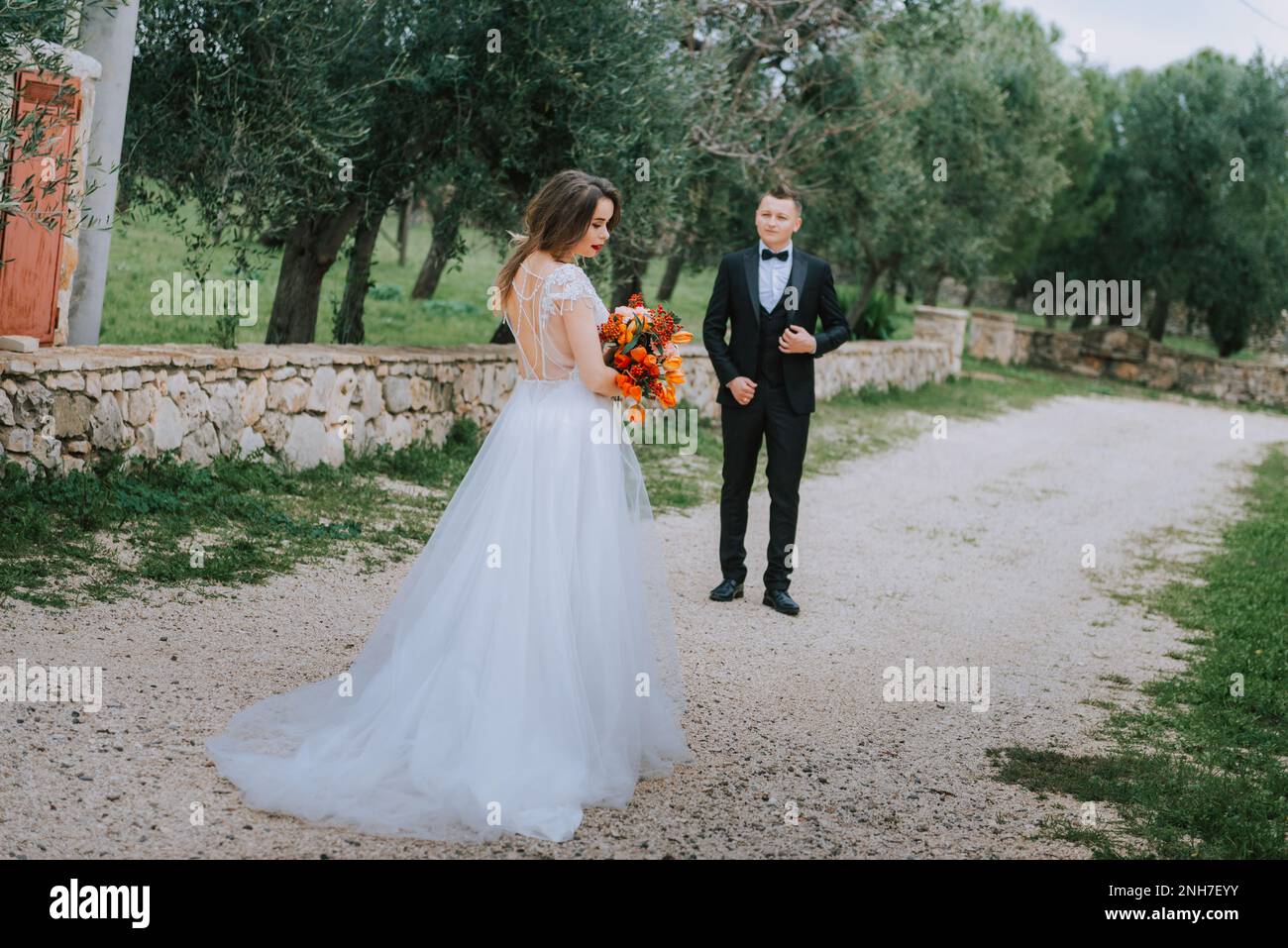 Felice coppia sorridente di stile che cammina in Toscana, Italia il giorno del matrimonio. La sposa e lo sposo camminano lungo la strada per le mani. Un giovane ed elegante co Foto Stock