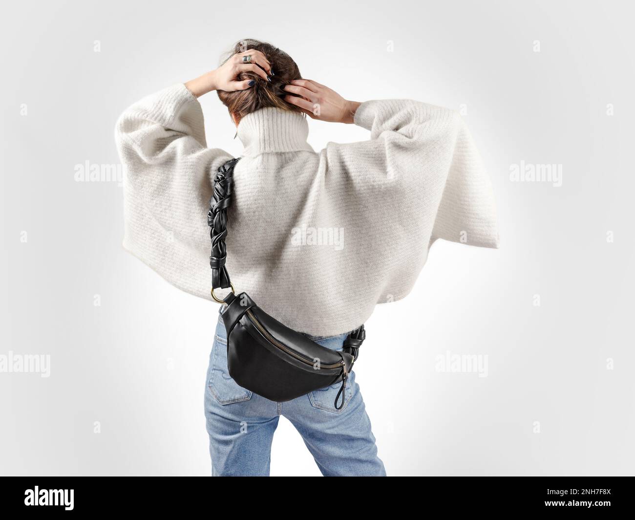 Donna irriconoscibile da dietro che indossa un pullover oversize bianco e un corpo a croce in vera pelle nera Fanny Pack. Look alla moda per la stagione invernale Foto Stock